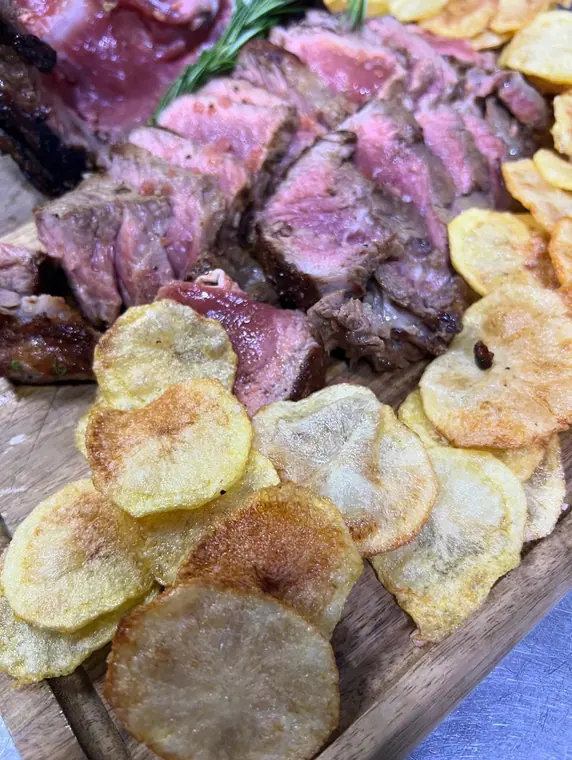 Close-up of sliced steak and fried potato slices on board
