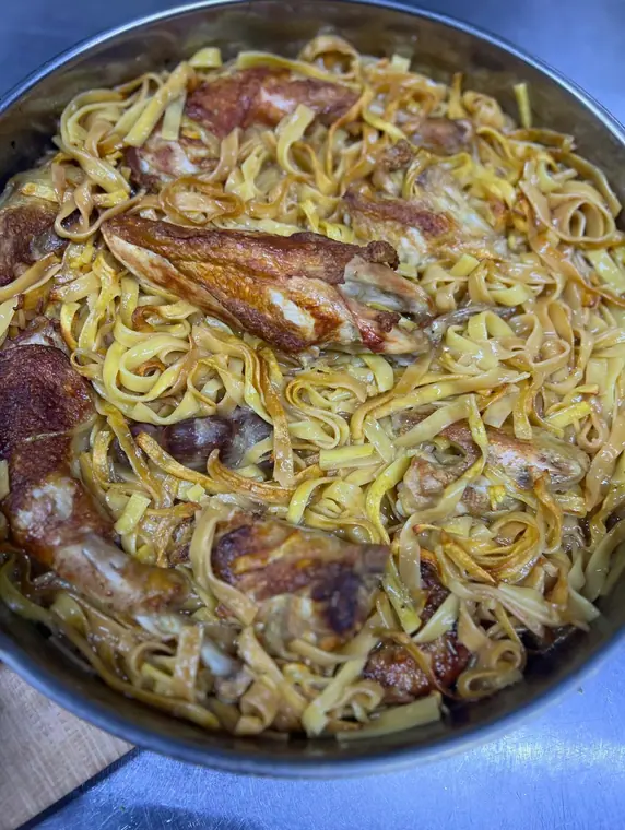 Close view of chicken wings over noodles in a pan
