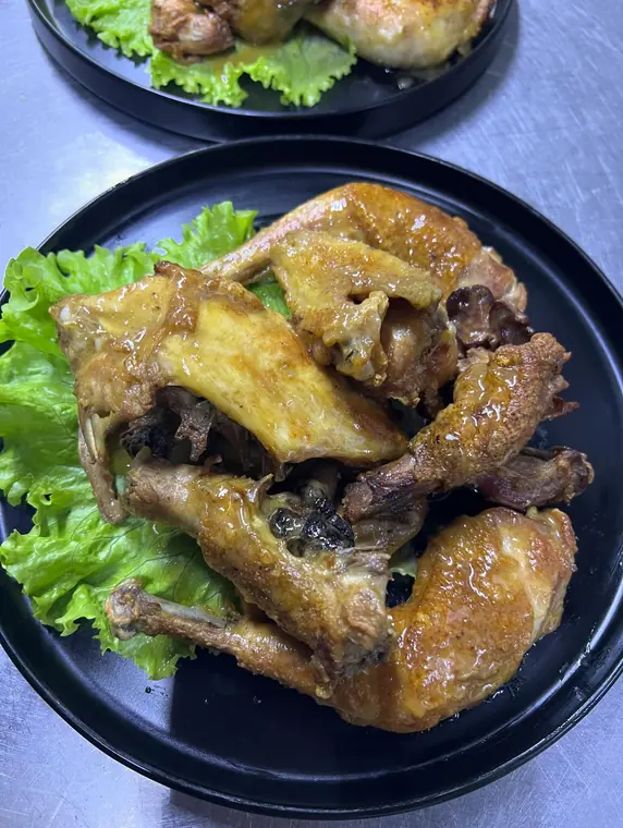 Close view of roasted chicken pieces on black plate with lettuce
