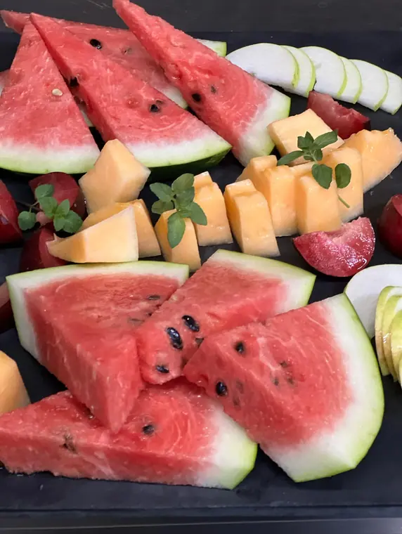 Close view of watermelon wedges, melon cubes and plum on dark board