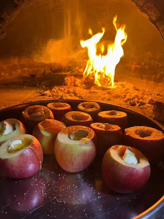 Cored apples filled with cheese in tray before wood-fired oven