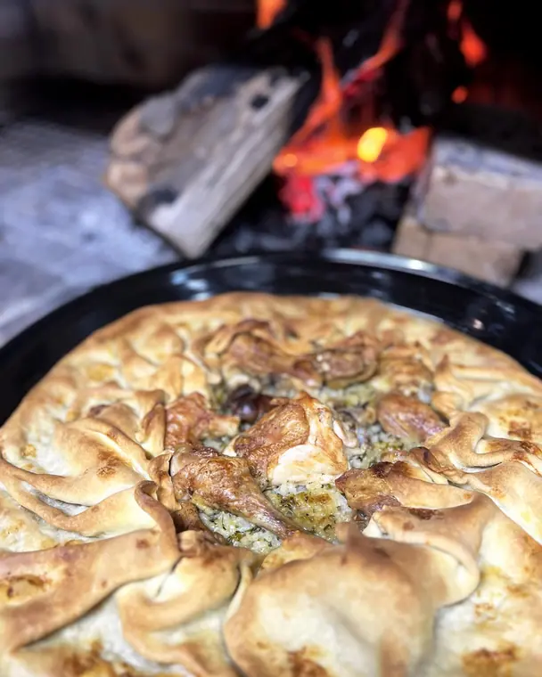 Filo pie with chicken pieces in round pan before a wood fire
