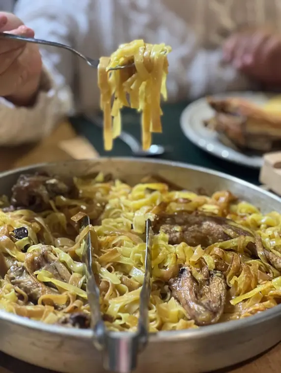 Fork lifting ribbon pasta above a serving pan at the table