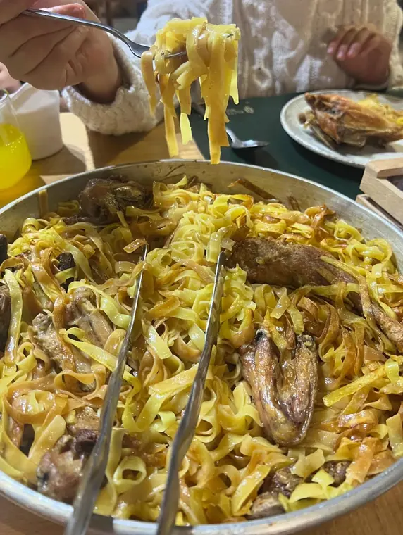 Fork lifting tagliatelle above metal pan on wooden table