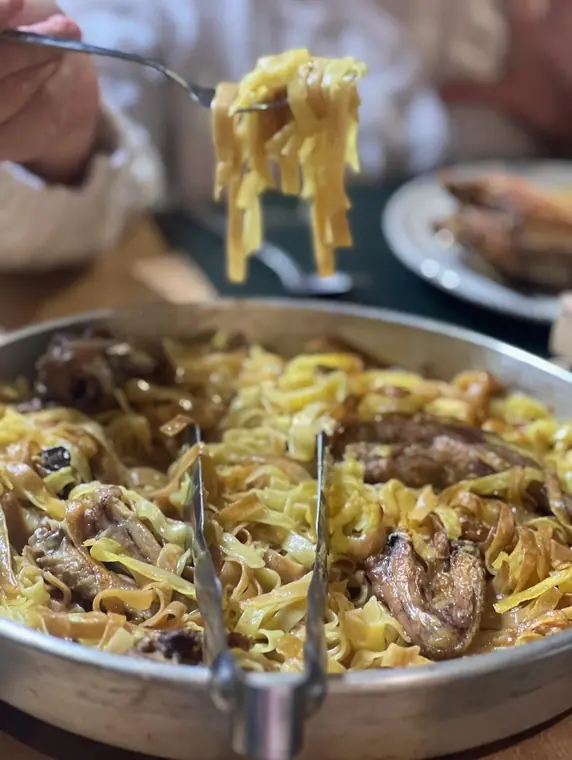 Fork of tagliatelle above pan, background out of focus