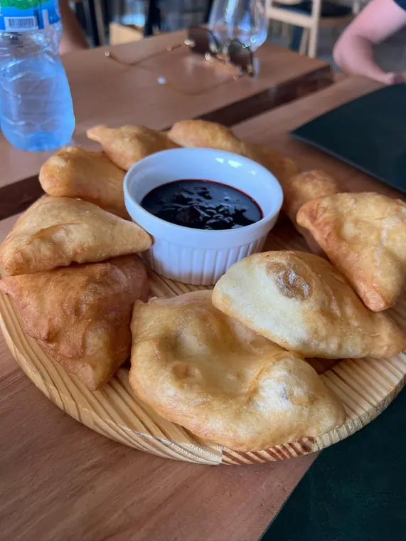 Fried dough pastries around bowl of dark jam on wooden board