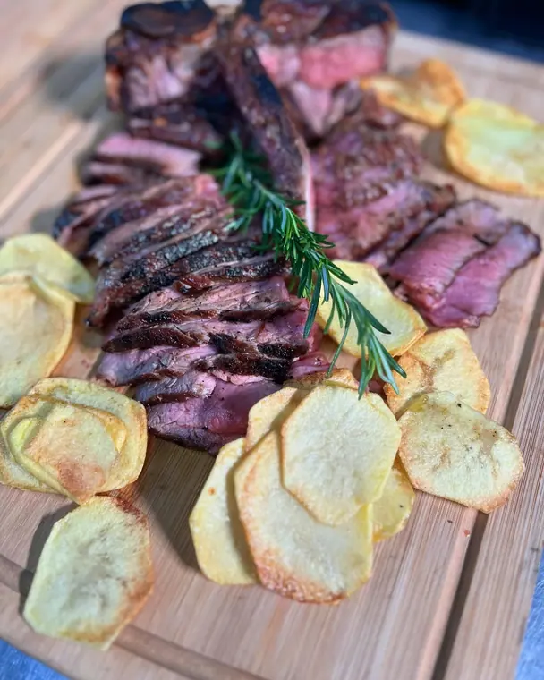 Low-angle view of sliced steak and potato crisps on wooden board