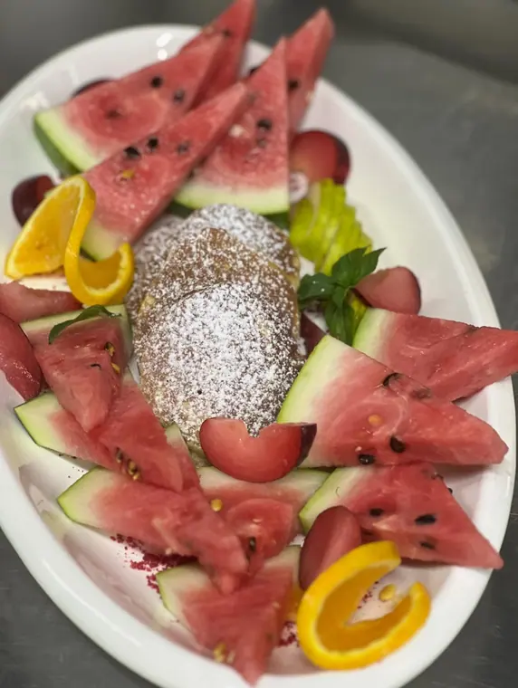 Oval plate with icing-dusted pancakes ringed by watermelon