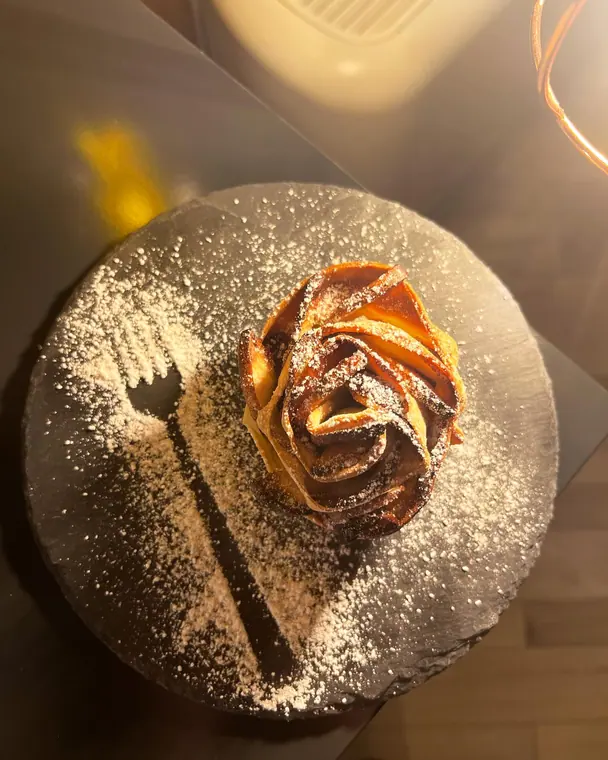 Overhead rose-shaped pastry on slate plate with sugar-dusted fork mark