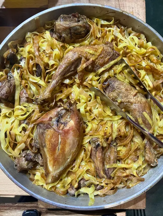 Pan of ribbon pasta with roasted poultry pieces and tongs