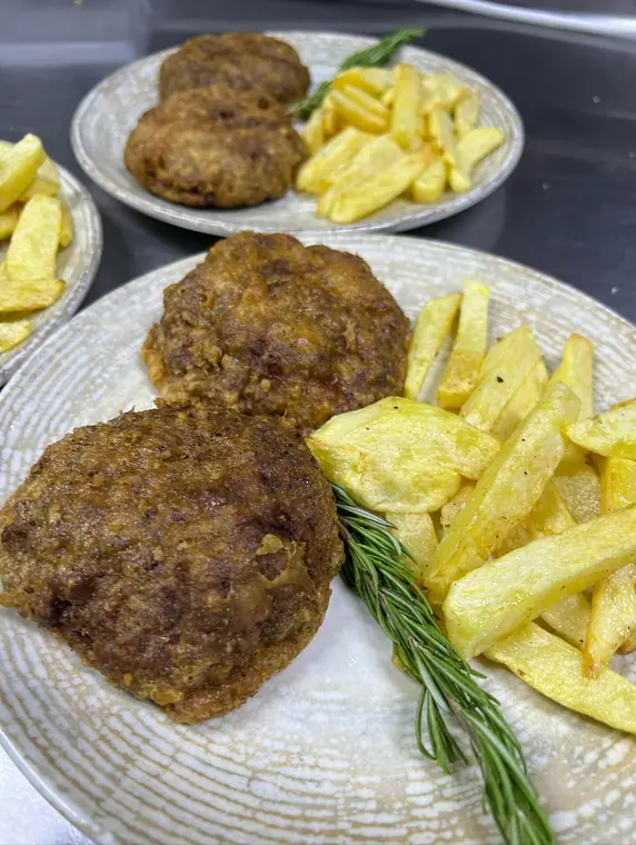 Plate of two fried meat patties with chips and rosemary