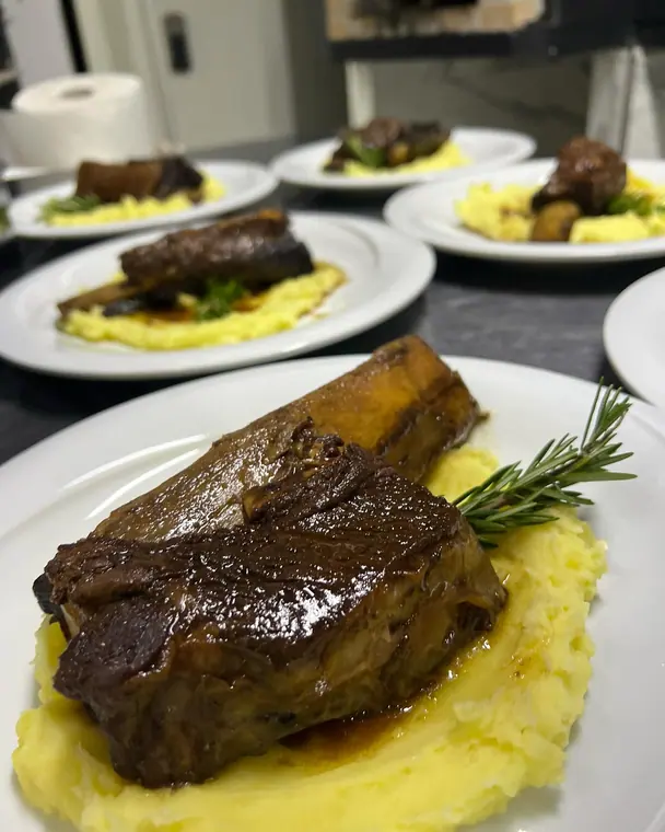 Plated short rib and mash with more plates behind in the kitchen