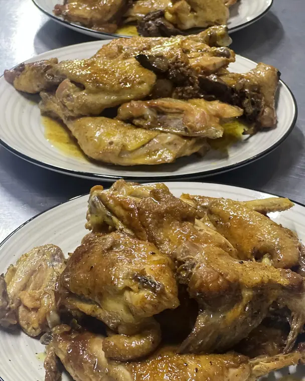 Plates of roasted chicken pieces in juices on steel counter