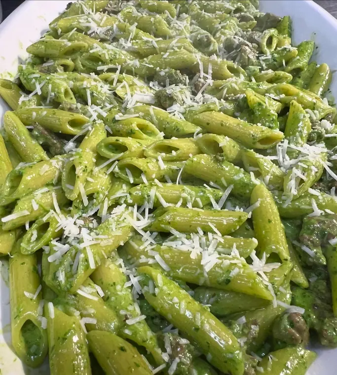Platter of penne in green pesto sauce with grated cheese