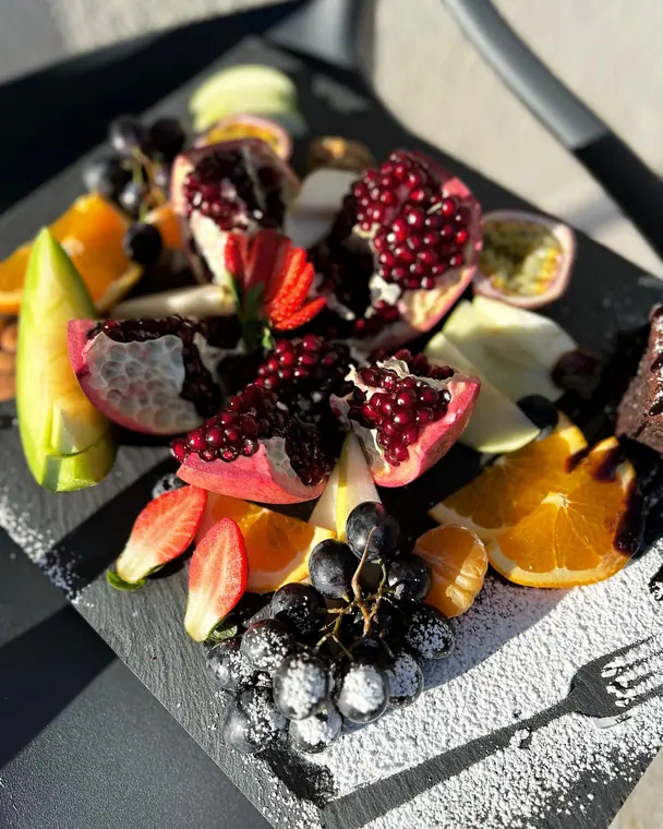 Pomegranate, citrus, grapes and strawberries on slate board in sunlight