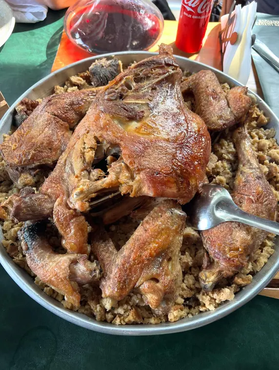 Roast poultry on bulgur in tray, carafe of red wine behind