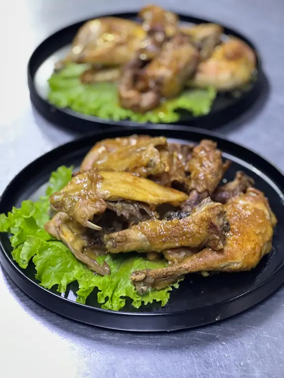 Roasted chicken pieces on black plates on steel counter