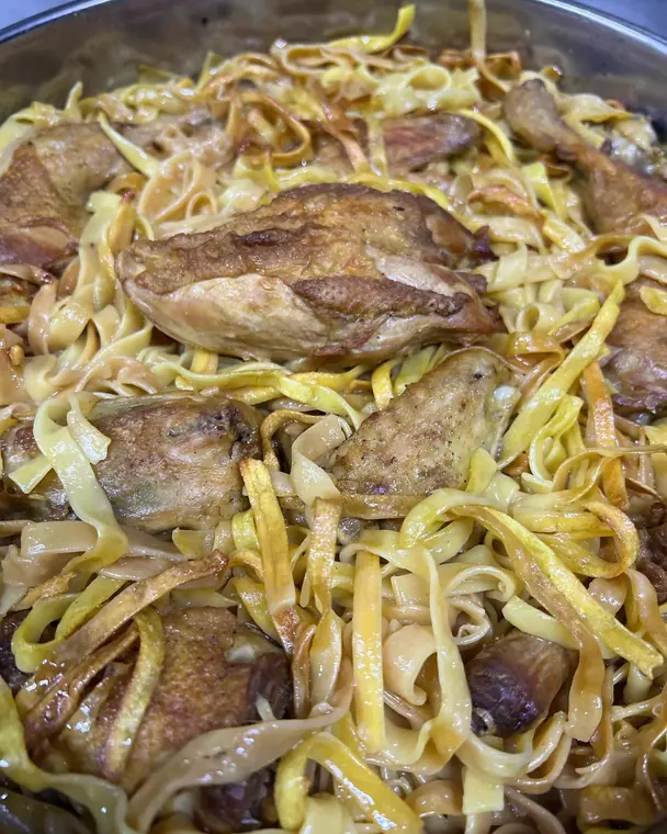 Roasted chicken pieces with flat egg noodles in metal tray