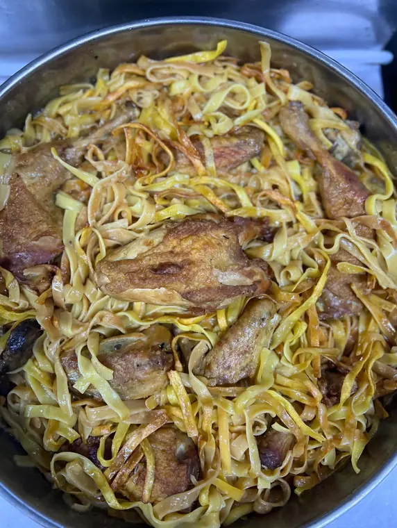 Roasted chicken pieces with flat egg noodles in metal tray