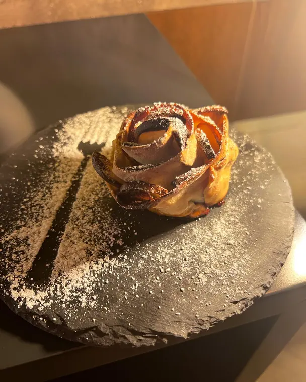 Rose-shaped pastry dusted with icing sugar on round slate plate