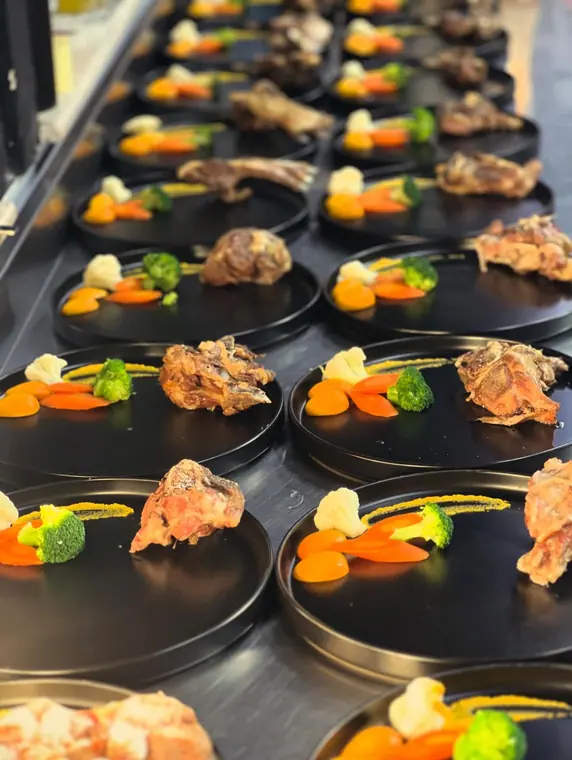 Rows of black plates with meat and vegetable garnish in kitchen