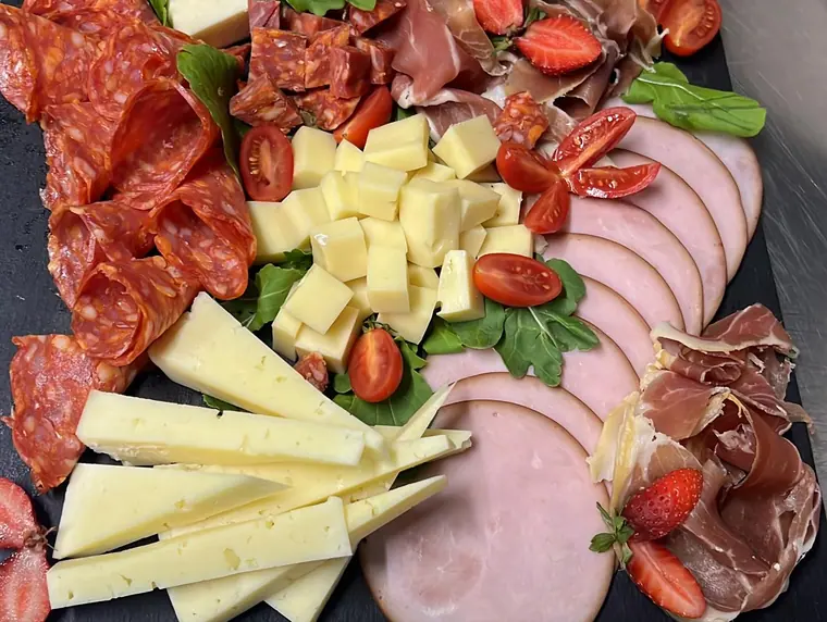 Slate board with cured meats, cheese cubes, tomatoes, strawberries