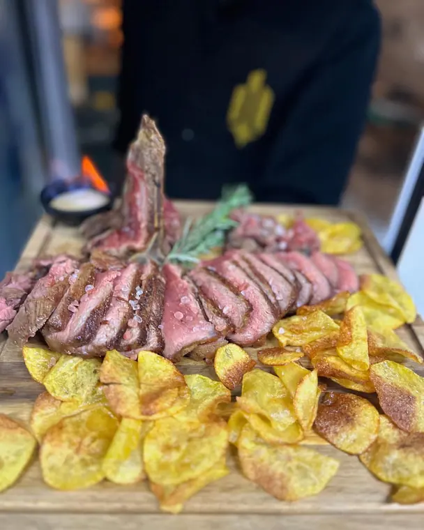 Sliced bone-in steak with potato crisps on a wooden board