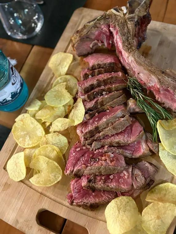 Sliced bone-in steak with rosemary and crisps on wooden board
