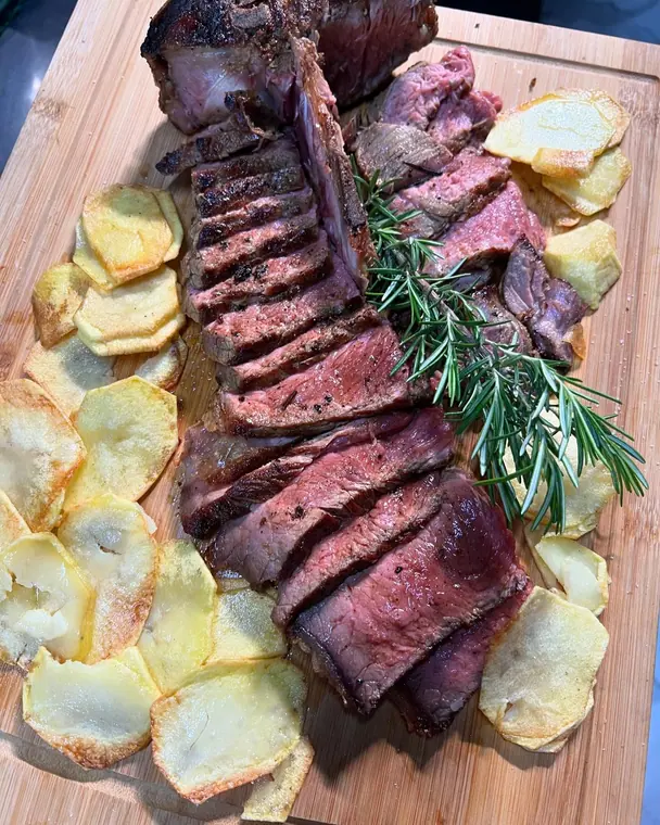 Sliced grilled beef on wooden board with potato slices and rosemary