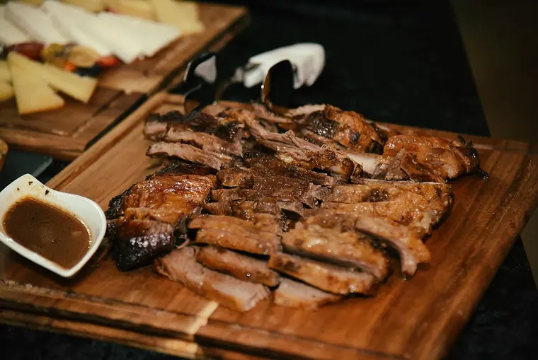 Sliced grilled meat on a board with sauce and cheese platter