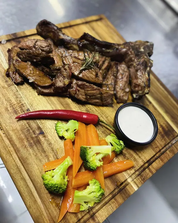 Sliced grilled steak on wooden board with vegetables and sauce
