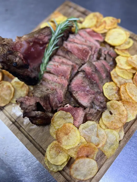 Sliced rare steak with fried potato rounds on wooden board