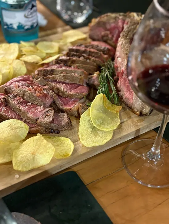 Sliced rare steak with rosemary and potato crisps on wooden board