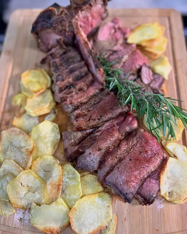 Sliced T-bone steak and fried potato rounds on wooden board