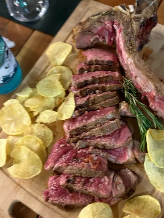 Sliced T-bone steak and potato crisps on wooden board