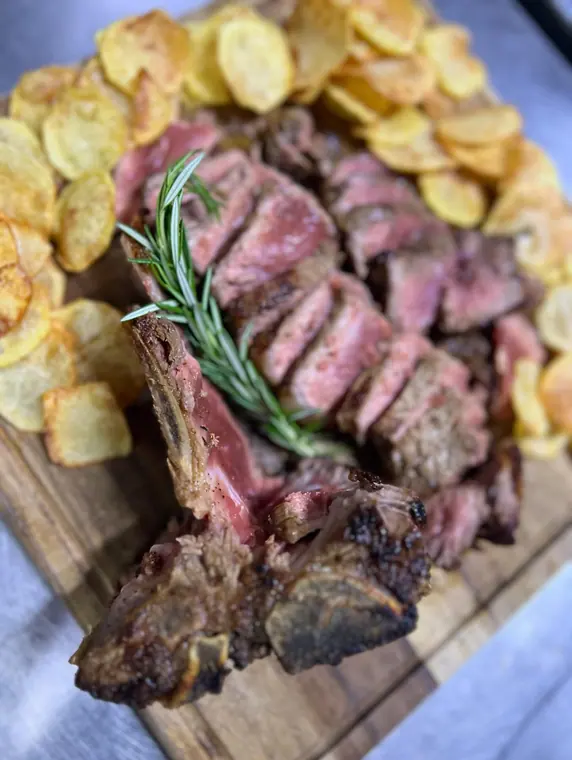 Sliced T-bone steak and potato crisps on wooden board