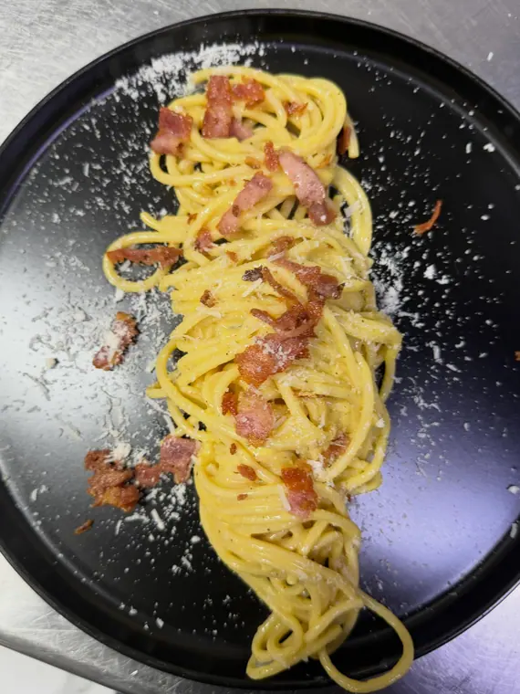 Spaghetti carbonara with bacon and grated cheese on black plate