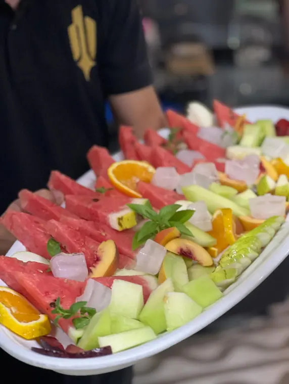Staff member holding mixed fruit platter with melon and ice