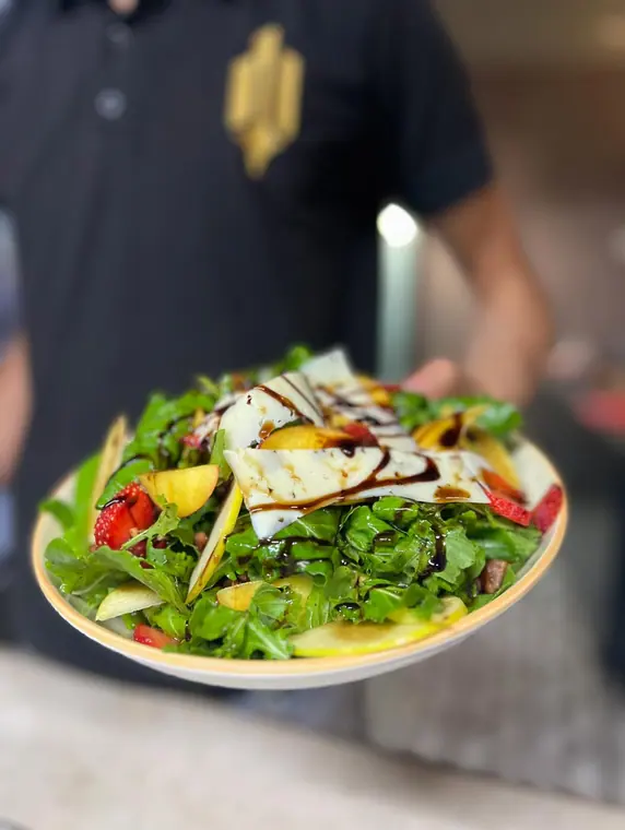 Staff member holding plated salad, head out of frame