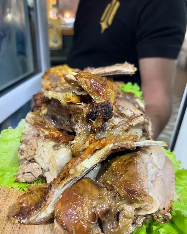 Staff member holds board of roast lamb on lettuce, torso only