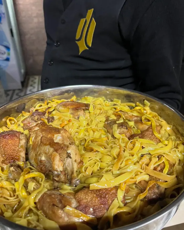 Staff member holds large tray of chicken with tagliatelle