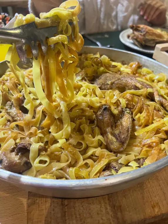 Tagliatelle with poultry in metal pan, tongs lifting pasta