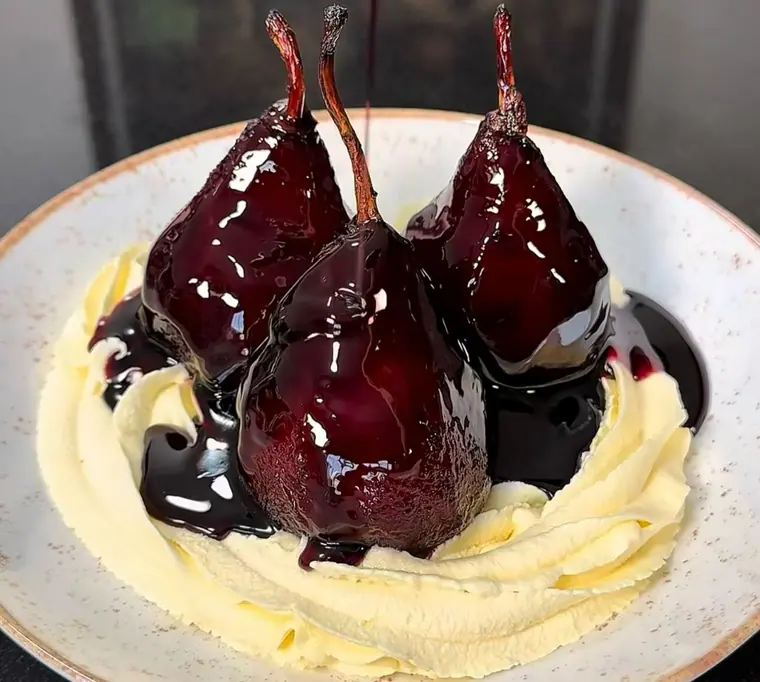 Three poached pears in dark red syrup on whipped cream