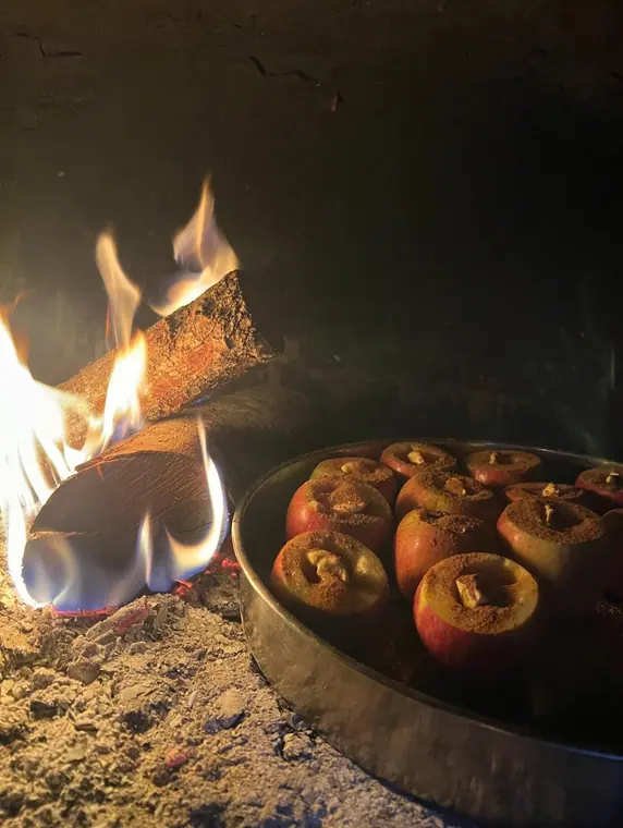 Tray of cinnamon-dusted apples beside burning logs in oven