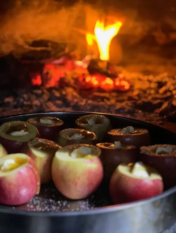Tray of stuffed apples beside embers in wood oven