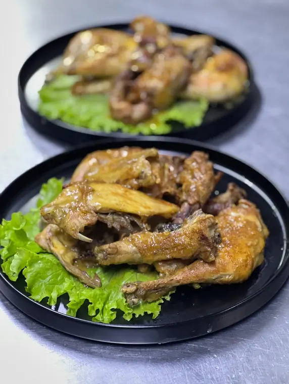 Two black plates of roasted chicken wings on lettuce