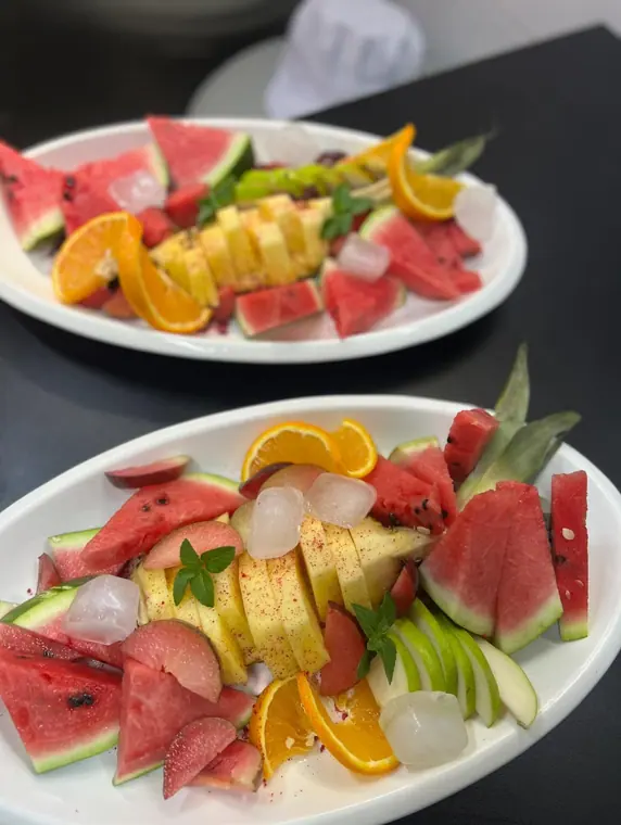 Two fruit plates on dark counter with chef hat behind