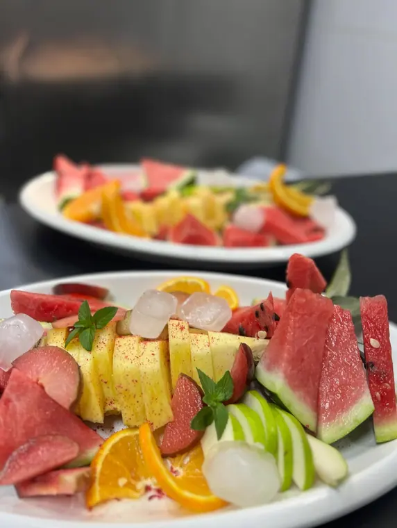 Two oval plates of sliced pineapple, watermelon and apple