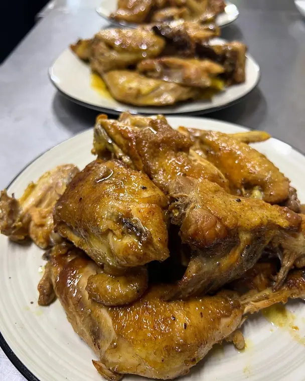 Two plates of glazed roasted chicken pieces on steel counter