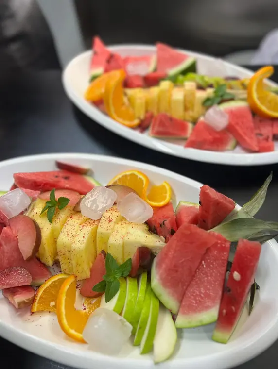 Two plates of pineapple, watermelon, apple and orange slices